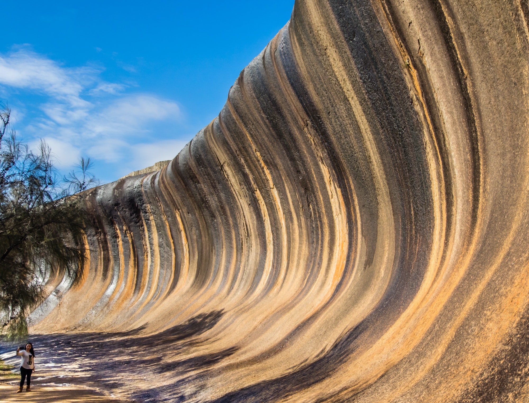 Wave Rock, Western Australia, with a woman taking a selfie in the bottom-left corner to show scale